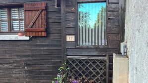 A rustic wooden building with a number '17' sign, a window with a view of trees, and a planter with purple flowers. - Gîte du Puy des Gardes (Meymac)