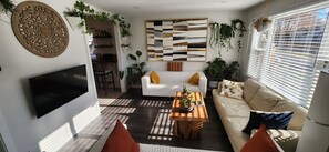 Un salon moderne doté d’un téléviseur à écran plat, d’une table basse en bois agrémentée de plantes, d’un canapé avec des coussins jaunes et d’un coin repas avec une table et des chaises en bois.