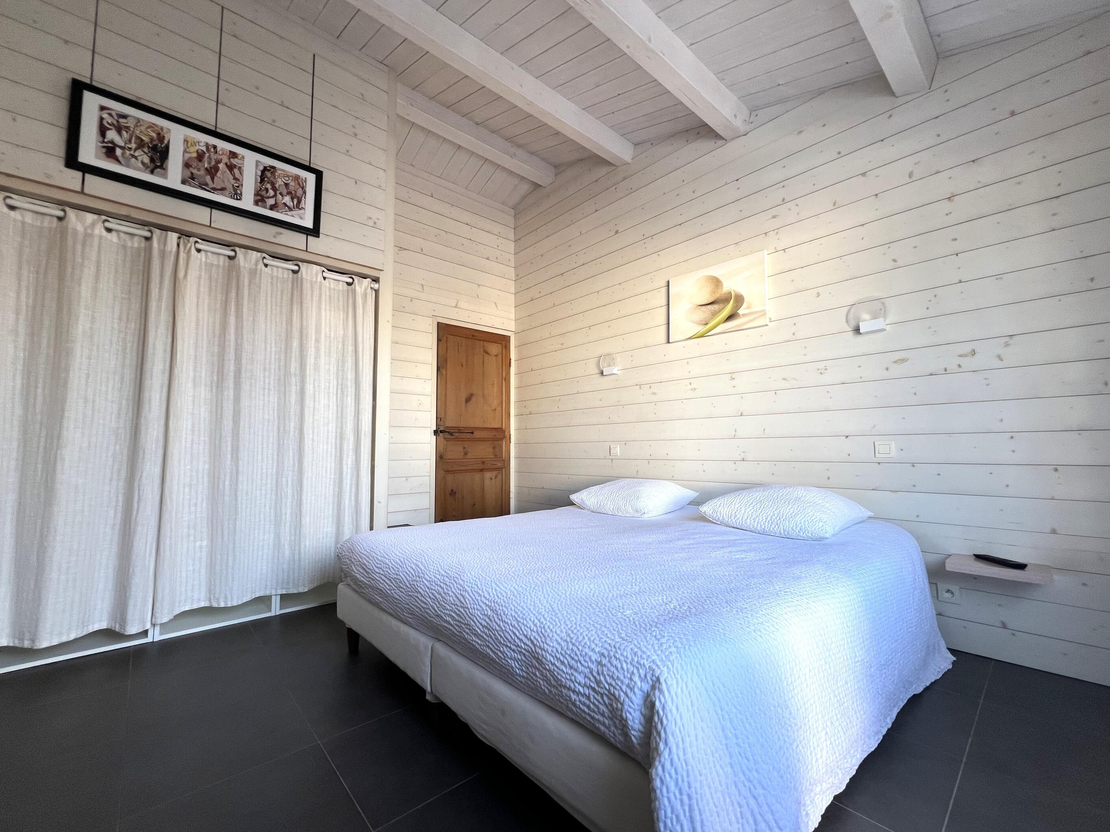 Une chambre à coucher avec un grand lit, des murs en bois, une porte et un tableau encadré accroché au mur.
