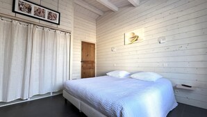 A bedroom with a large bed, wooden walls, a door, and a framed picture on the wall. - House RIVAGE       . (Sainte-Marie-de-Ré)
