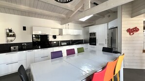 A modern kitchen with white cabinetry, a black countertop, and a large island with colorful chairs. - House RIVAGE       . (Sainte-Marie-de-Ré)