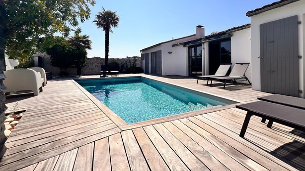 A swimming pool with a wooden deck, lounge chairs, and a palm tree. - House RIVAGE       . (Sainte-Marie-de-Ré)