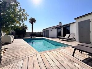 A swimming pool with a wooden deck, lounge chairs, and a palm tree. - House RIVAGE . (Sainte-Marie-de-Ré)