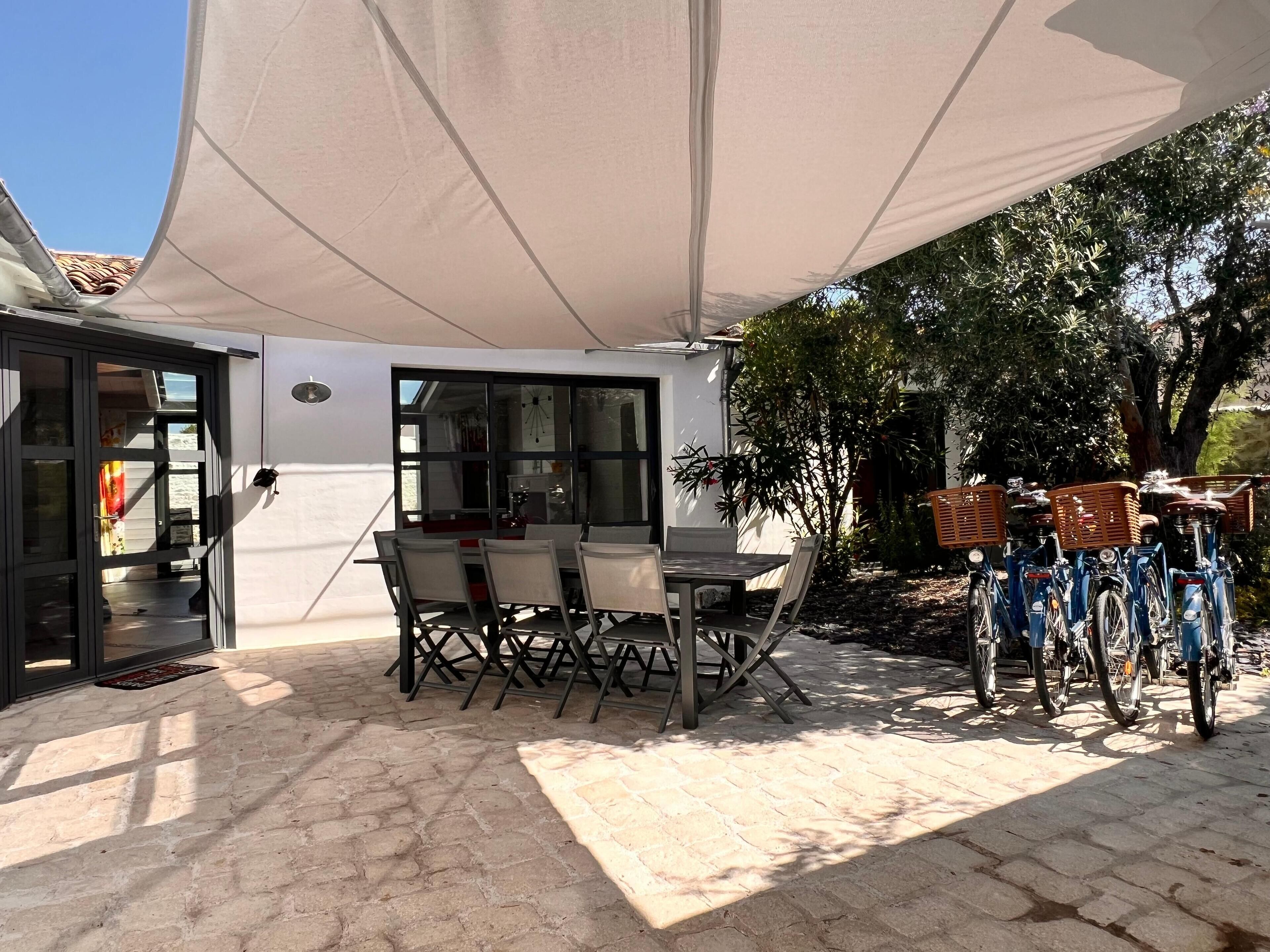 An outdoor patio with a table and chairs under a large canopy, a bicycle rack, and a view of a building with a tiled roof.