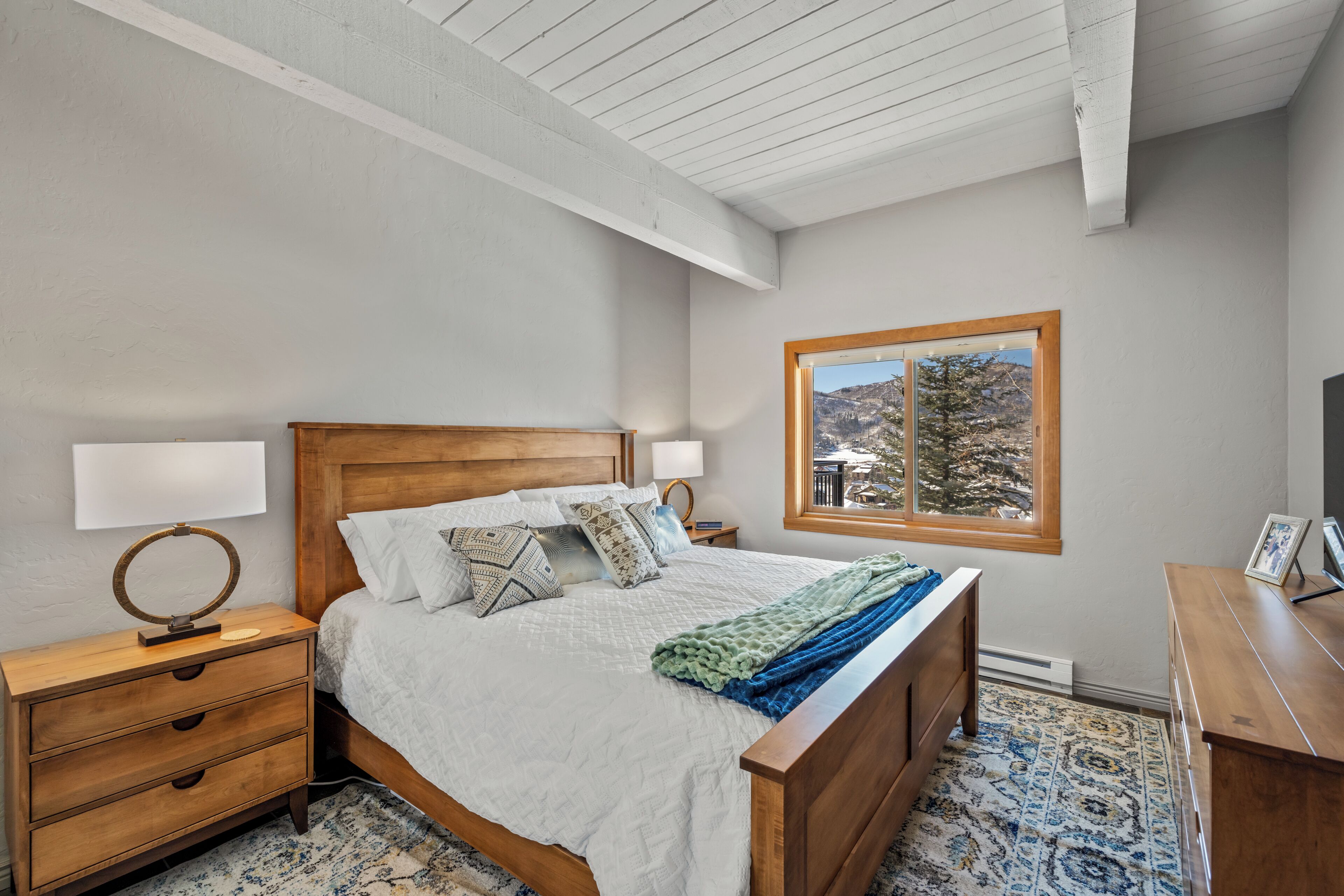 A bedroom with a wooden bed, bedside tables, a window with a view, and a patterned rug.
