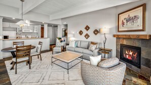 Una sala moderna con chimenea, un comedor con mesa y sillas, y una cocina al fondo.