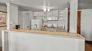 Una cocina con armarios blancos, encimera de granito, refrigerador, estufa y microondas.