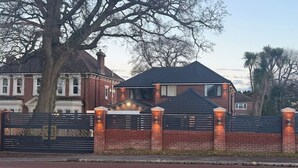 A residential house with a brick exterior, a black metal gate, and a large tree in the background. - Peace house suite

 (Waterlooville)