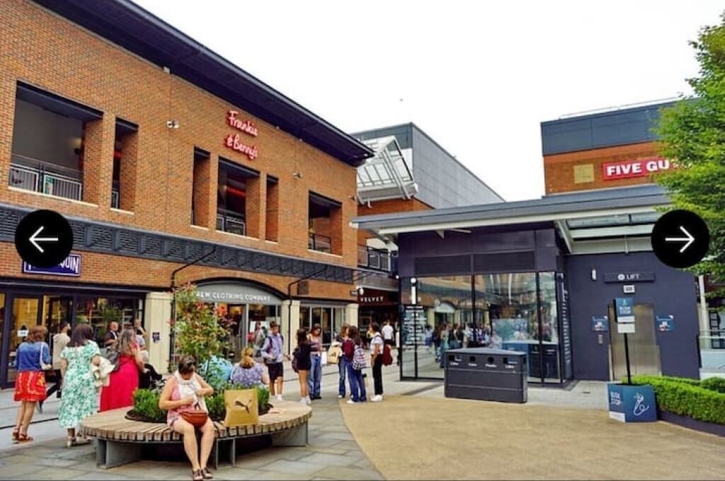 A shopping area with a brick building, a seating area, and a modern entrance.