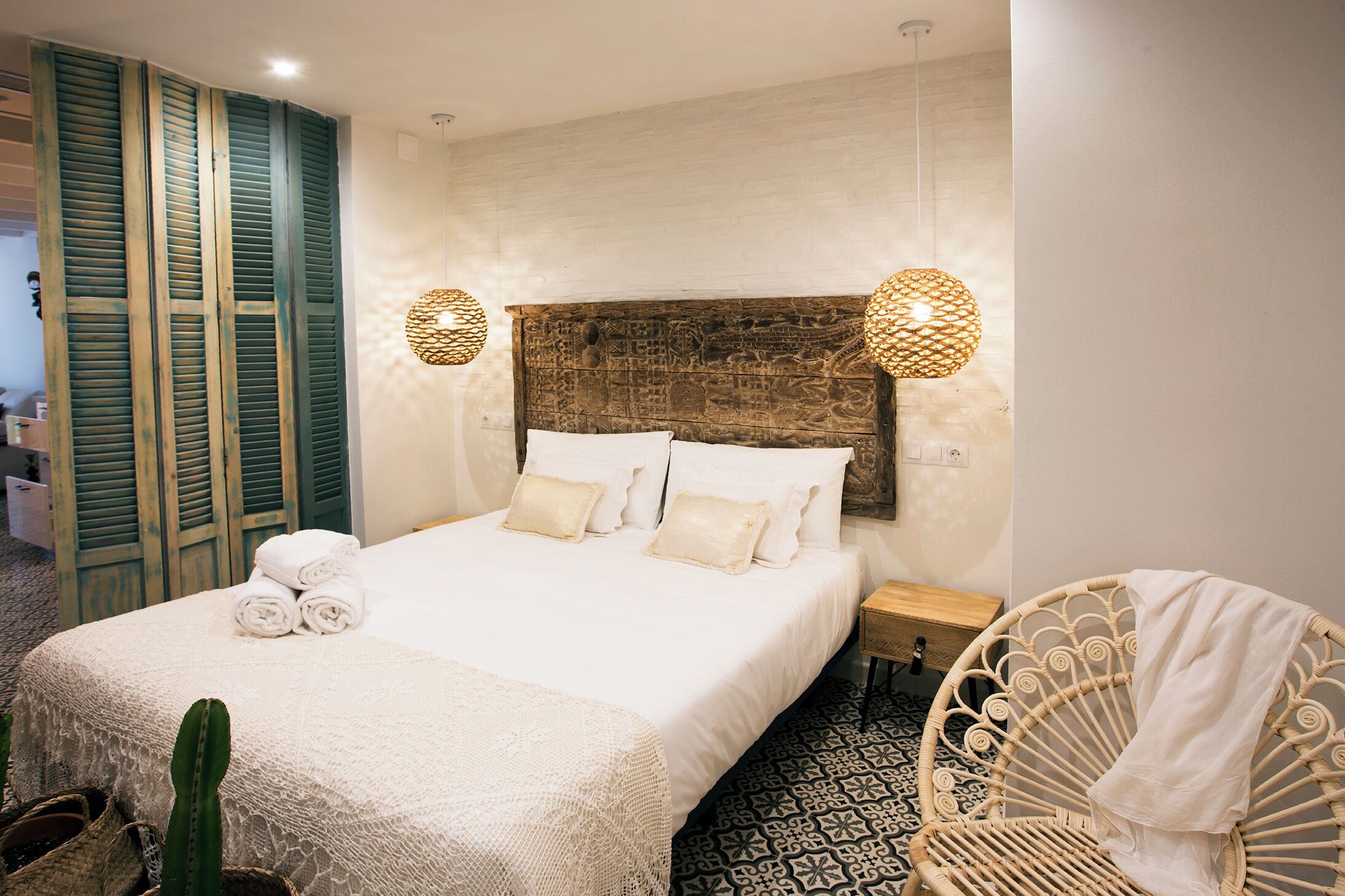 Una cama bien hecha con sábanas y almohadas blancas, una silla de mimbre y un suelo con diseño.