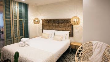 Una cama bien hecha con sábanas y almohadas blancas, una silla de mimbre y un suelo con diseño.