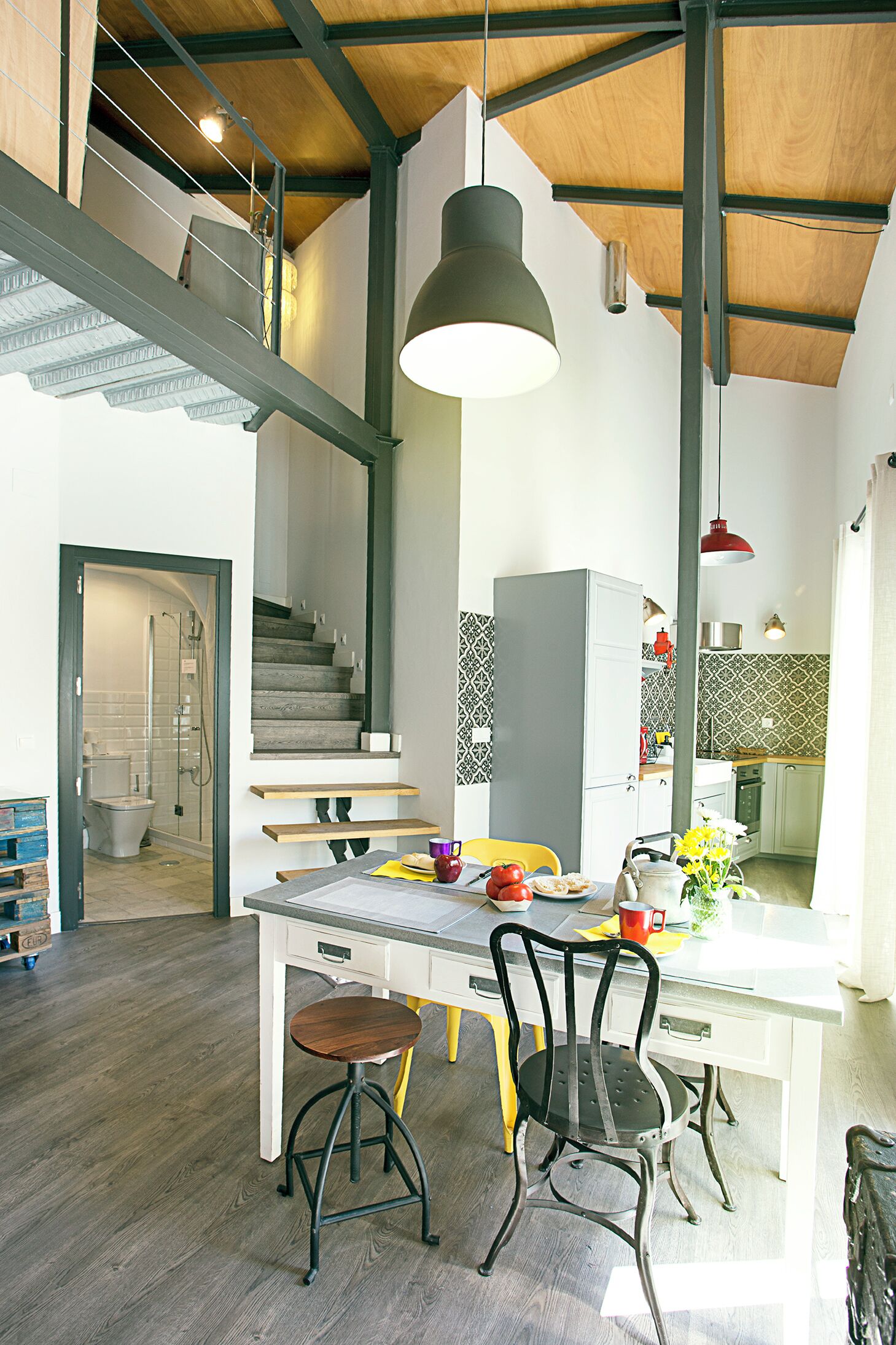 A modern kitchen with a dining area, wooden beams, and a staircase.