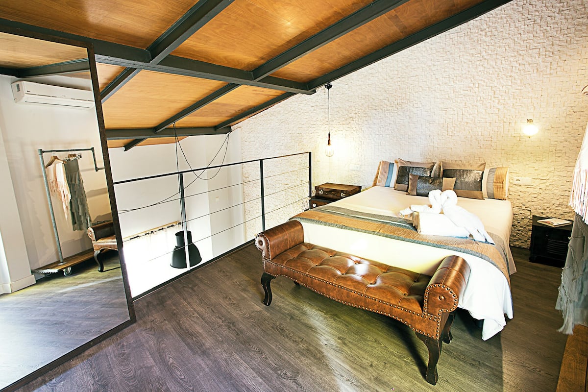 A bedroom with a bed, a bench, a mirror, and a stone wall.
