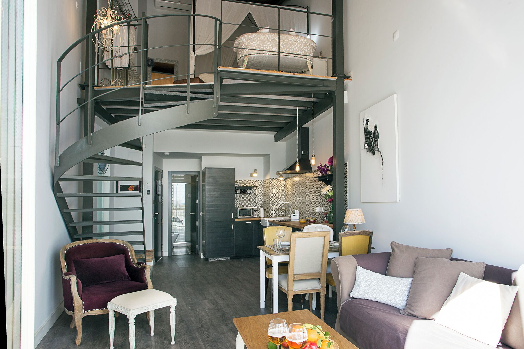 A modern loft apartment with a spiral staircase, a dining area, and a living room with a sofa and armchairs.