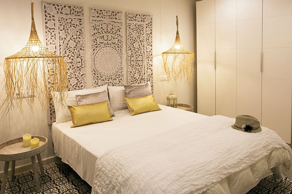 A neatly arranged bedroom with a large bed, two bedside tables, decorative wall panels, and hanging light fixtures.