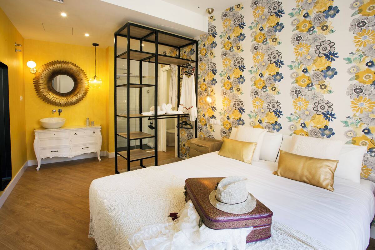 A hotel room with a bed, a white dresser, a mirror, and a shower area.