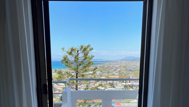 Apertura di una porta che dà su un balcone con vista su una cittadina costiera e un albero.