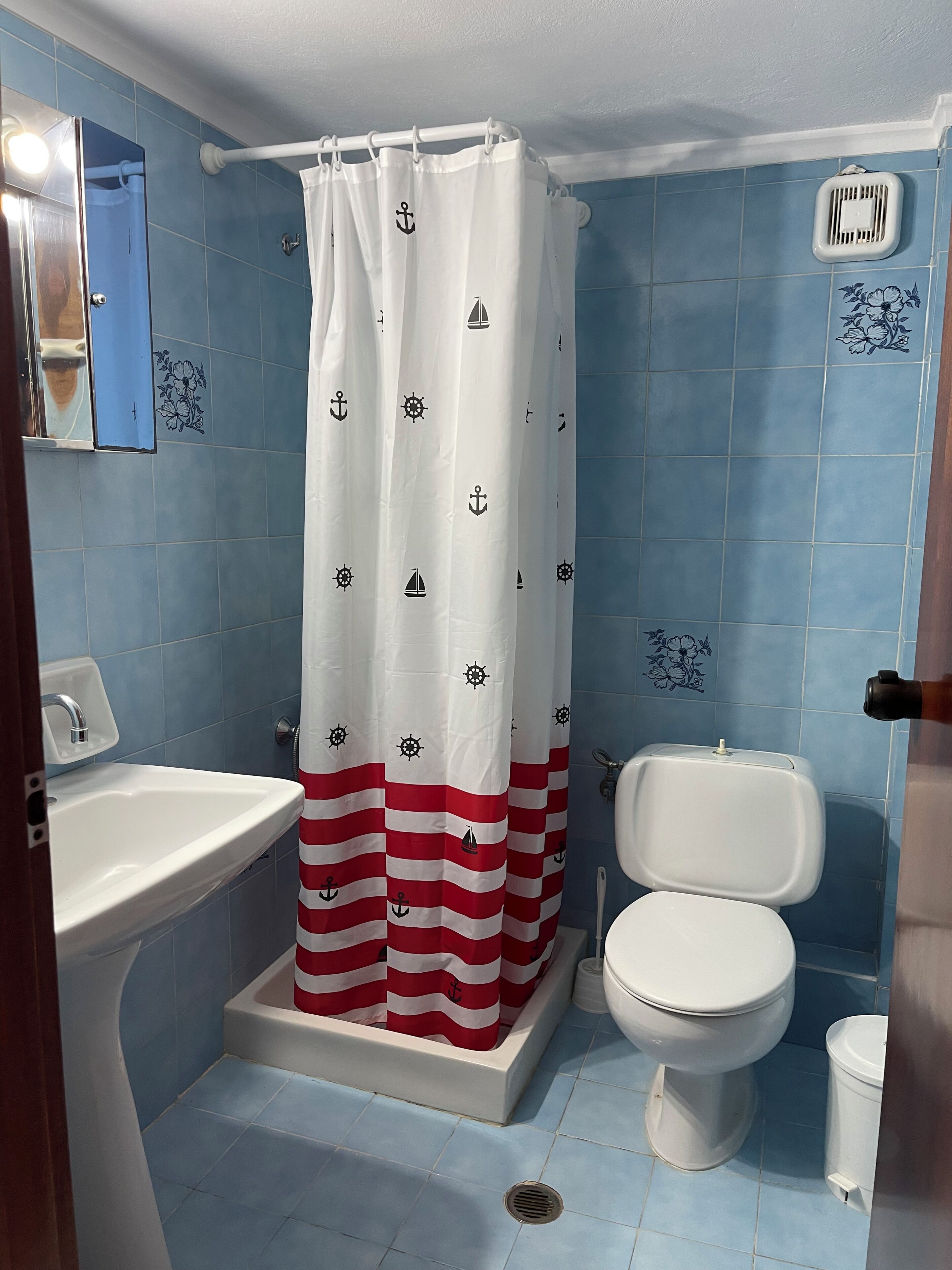 A bathroom with a shower curtain featuring nautical designs, a white sink, a toilet, and blue-tiled walls.