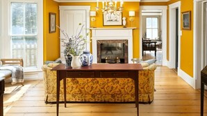 A dining area with a wooden table, patterned chairs, a vase with flowers, and a fireplace.