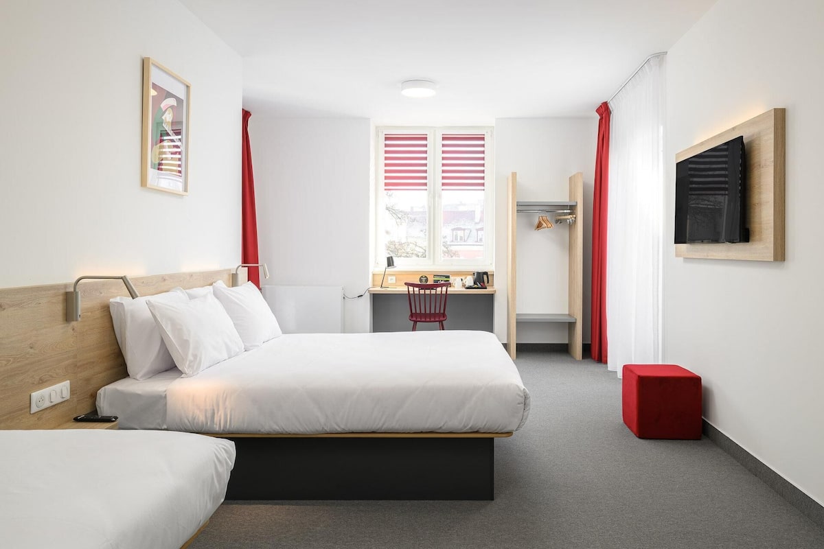 A modern hotel room with a bed, a desk, and a chair.