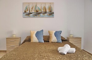 A bedroom with a bed, two nightstands, a painting of sailboats, and a towel on the bed. - Apartamento Dúplex Bahia Sur (SAN FERNANDO)