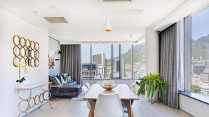 Un comedor moderno con una larga mesa, sillas blancas y vistas a la ciudad a través de grandes ventanales.