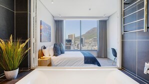 Una habitación de hotel moderna con una cama grande, vistas a la ciudad y una bañera.