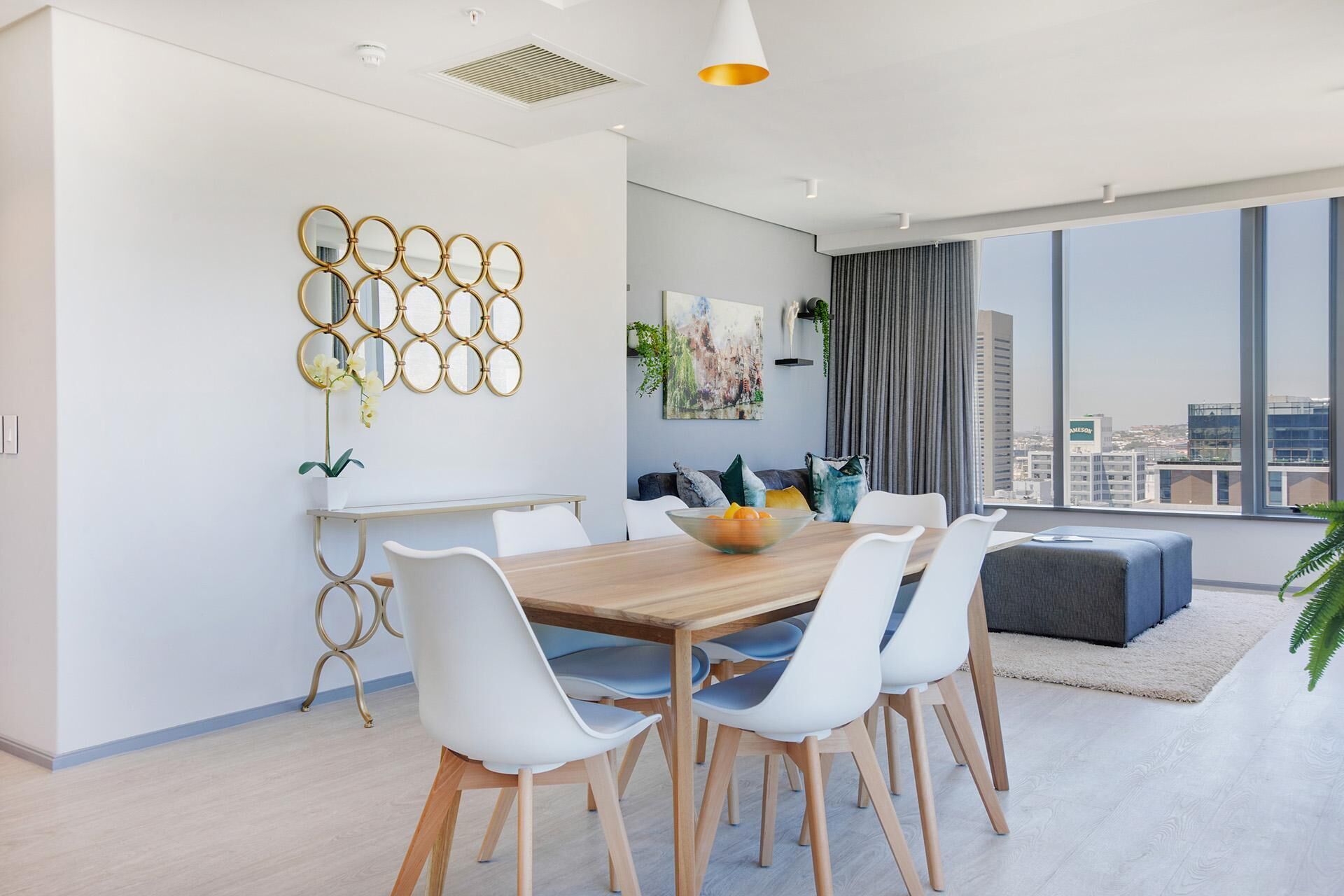 A modern dining area with a wooden table, white chairs, and a decorative mirror wall.