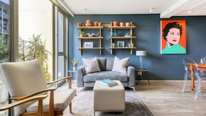 Un salon moderne avec un canapé gris, une chaise en bois, une petite table et une bibliothèque agrémentée d’objets décoratifs.