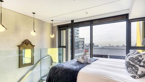 Une chambre d’hôtel moderne avec un grand lit, une rambarde en verre et une vue sur la ville.