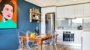 Une cuisine moderne avec une table à manger en bois, des chaises transparentes, un réfrigérateur en acier inoxydable et un lave-vaisselle.