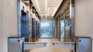 Un vestíbulo moderno de ascensor con puertas metálicas y un papel tapiz decorativo al fondo.