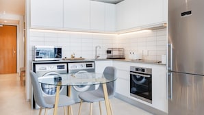 Una cocina moderna con armarios blancos, una mesa de comedor de vidrio y electrodomésticos de acero inoxidable.