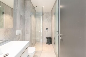 A modern bathroom with a glass shower enclosure, a white sink, and a toilet.