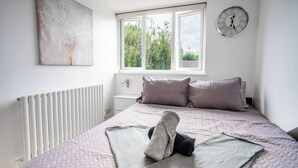 A bedroom with a bed, a window, a radiator, a clock, and a painting on the wall. - Luxury 3 Bed Shard View House! Private parking,Garden, on Door step of the city! (London)