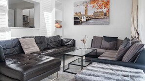 Una sala moderna con un sofá de cuero negro, una mesa de centro de vidrio y un cuadro grande con una vista de la ciudad.