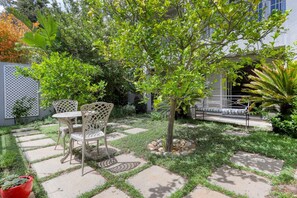 A patio area with a table and chairs, surrounded by a garden with various plants and a small tree. - French Country Cottage on Table Mountain (CAPE TOWN)