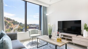 Un salon moderne doté d’un grand téléviseur, d’un canapé, d’une table basse et offrant une vue sur le paysage urbain.