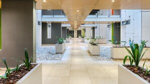 Un couloir intérieur moderne, doté d’un sol carrelé, de jardinières rectangulaires contenant des plantes et d’un plafond en bois.