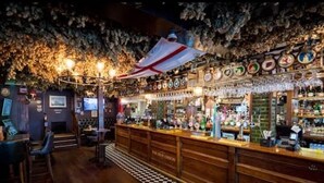 En bar med träinredning, ett stort utbud av flaskor och ett tak som är dekorerat med lövverk och en flagga.