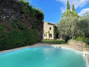 A swimming pool with a stone building in the background, surrounded by lush greenery.