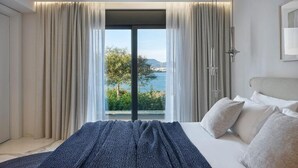 Ein Schlafzimmer mit großem Fenster, einem Bett mit weißer Bettwäsche und Meerblick.