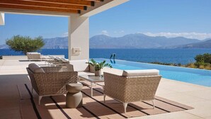 Ein Poolbereich mit Korbmöbeln und Blick auf das Meer und die Berge.