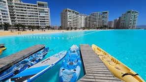 A beachside hotel with a pool, kayaks, and a clear blue sky.