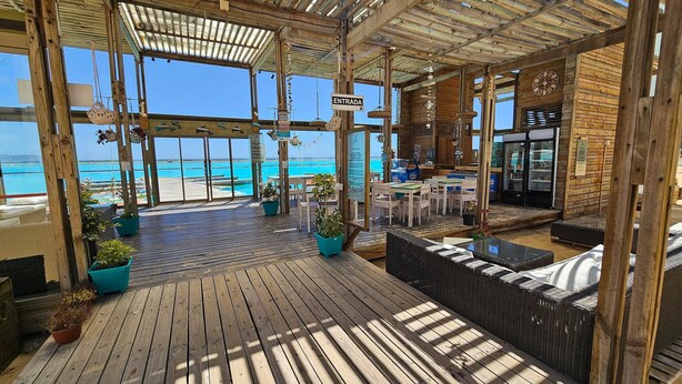 A wooden deck with a view of the ocean, a sign reading 'ENTRADA', and a seating area with tables and chairs. - Oceana Suites Laguna del Mar (La Serena)