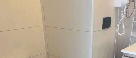 Un baño con inodoro, zona de ducha y secador de manos.