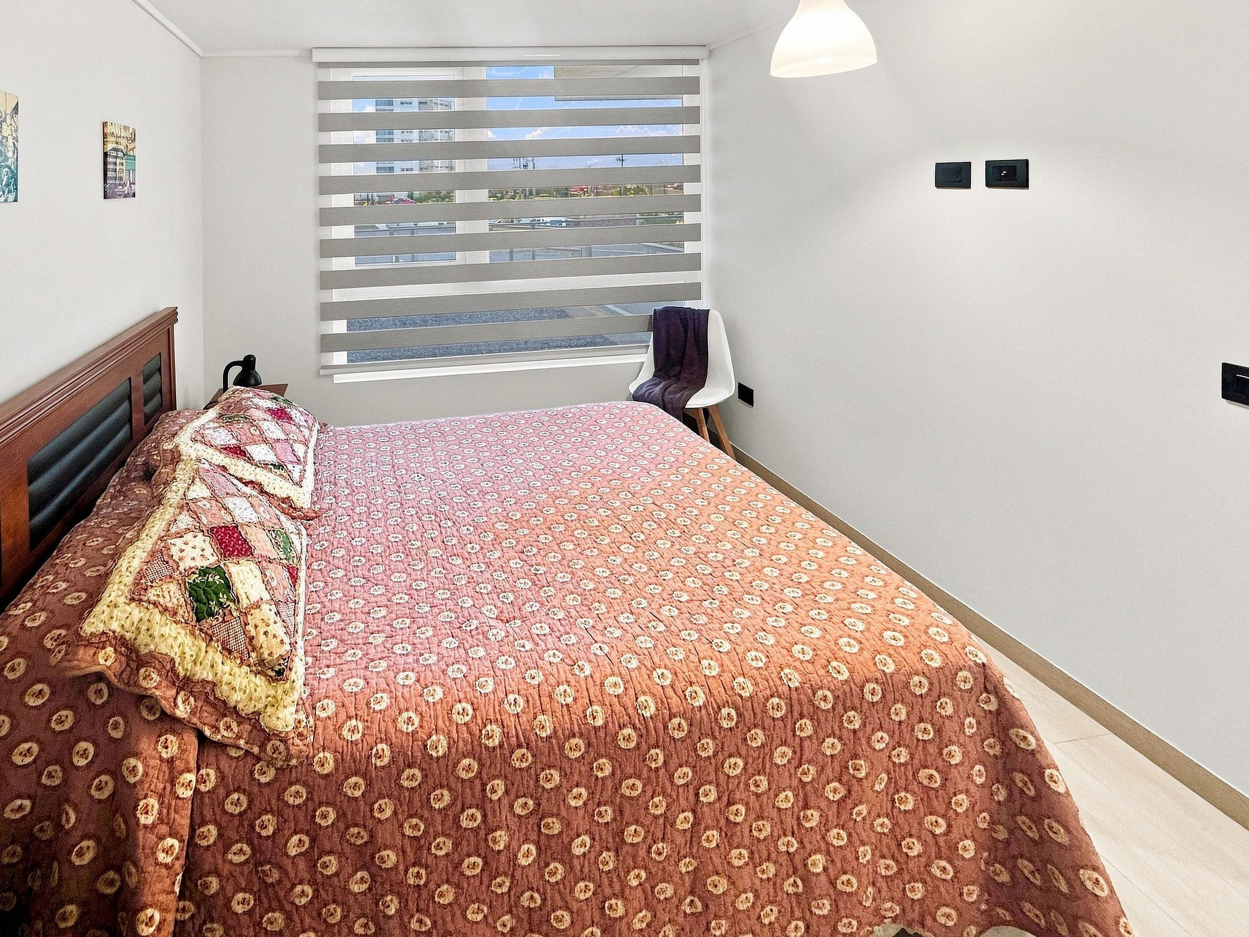 Un dormitorio con cama, ventana con persianas y una silla.