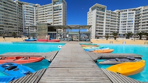 Ein Poolbereich mit mehreren Kajaks, einer Holzterrasse und Hochhäusern im Hintergrund.