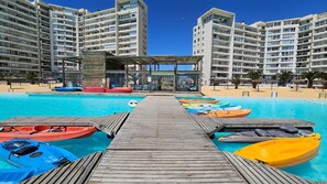 A pool area with multiple kayaks, a wooden deck, and high-rise buildings in the background. - Oceana Suites Laguna del Mar (La Serena)