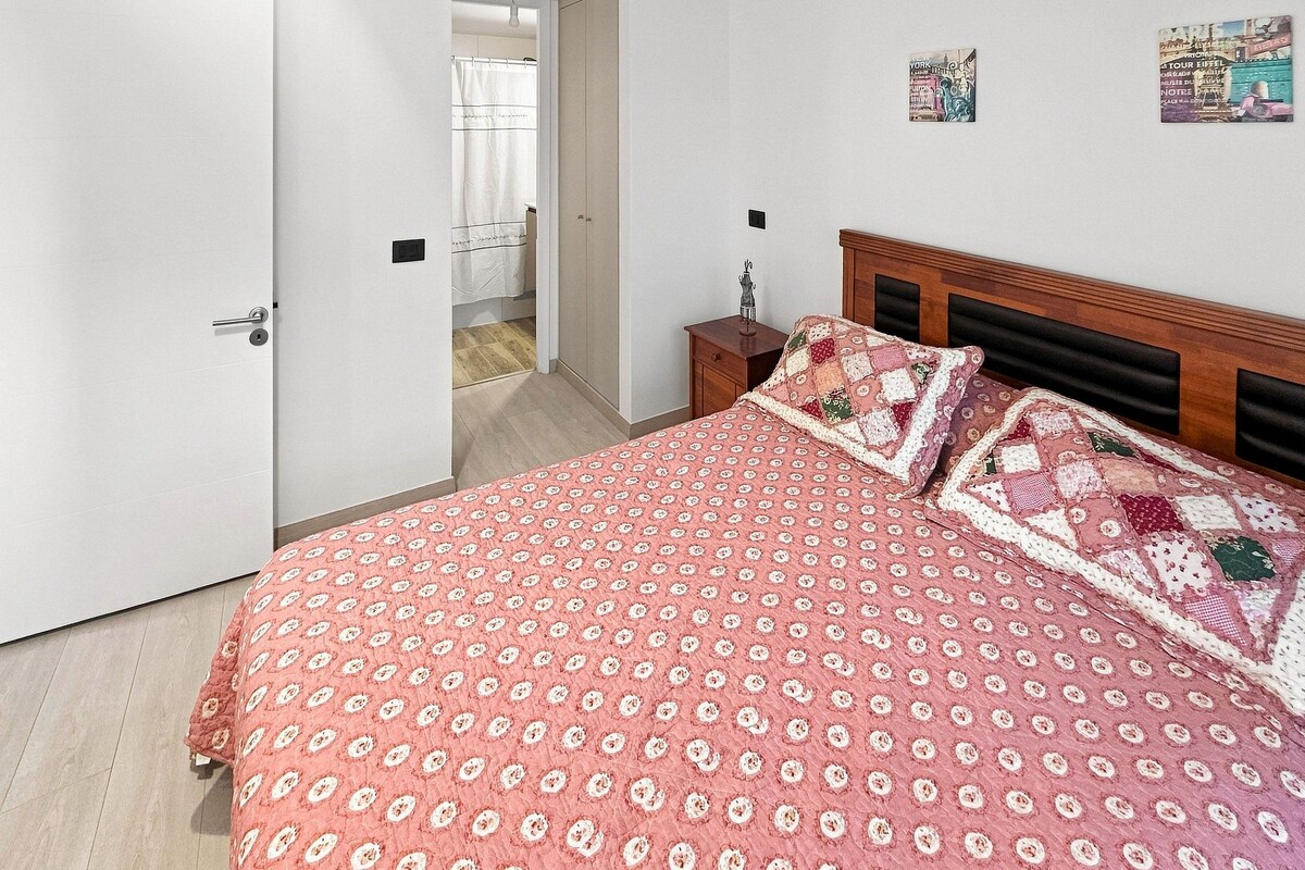 A bedroom with a bed, a nightstand, a door, and a wall with a poster.